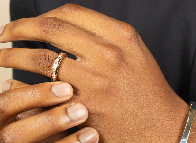 A close up of a mans hand wearing a slim geo eternity ring. Made in white gold and diamonds he is also wearing a silver snap bangle.